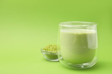 Glass of tasty matcha smoothie and powder on green background, closeup. Space for text