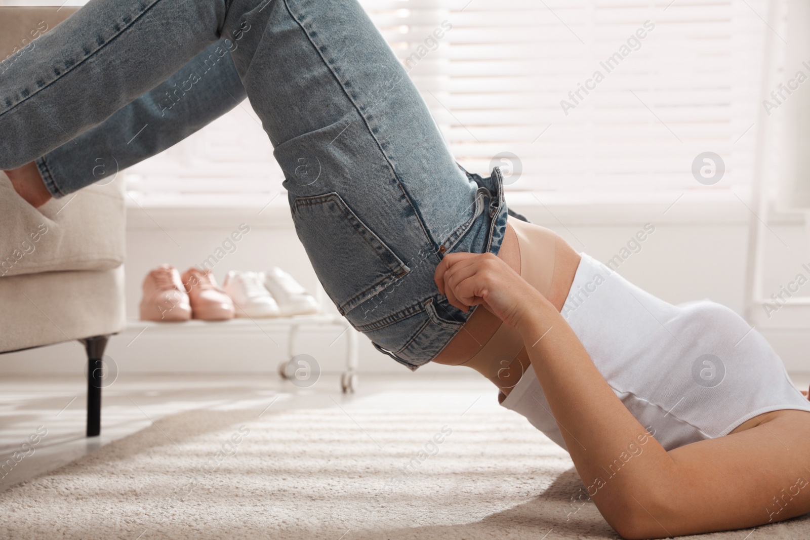 Photo of Woman struggling to squeeze into tight jeans while lying on floor at home, closeup