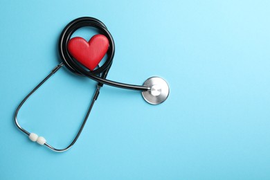 Stethoscope and red heart on light blue background, top view