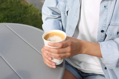 Photo of Coffee to go. Woman with paper cup of drink at grey table outdoors, closeup