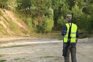 Man with hunting rifle wearing safety vest outdoors, back view. Space for text