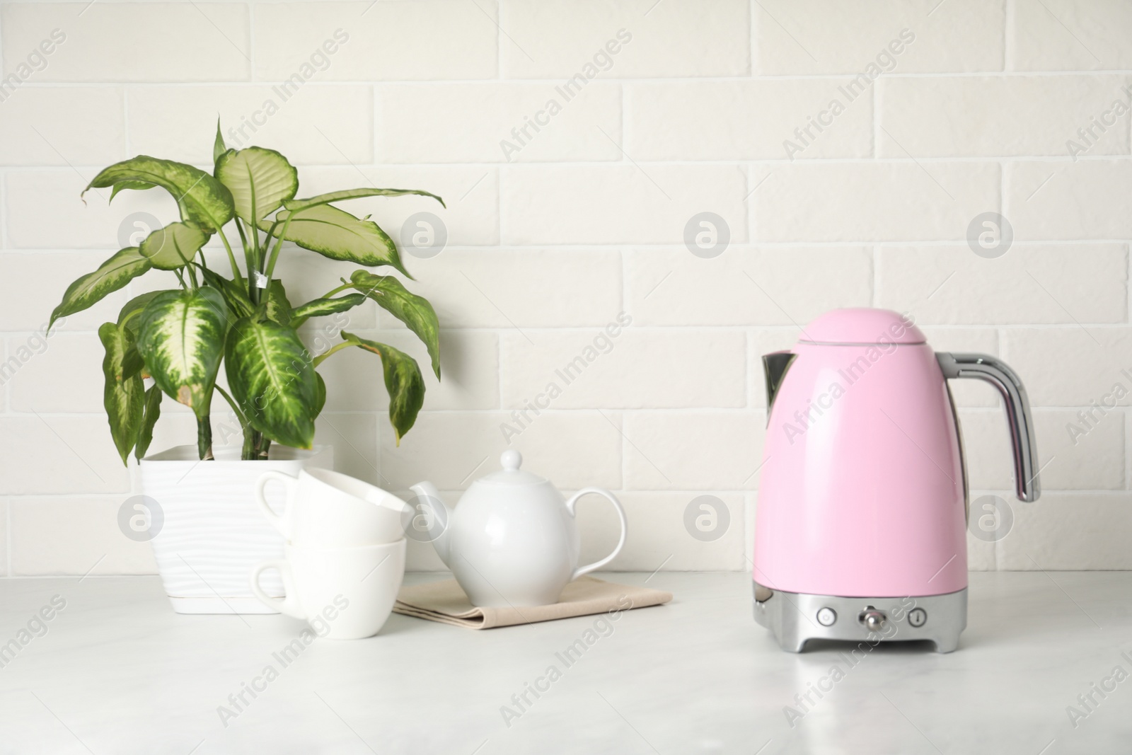 Photo of Modern electric kettle, houseplant and tea set on counter in kitchen