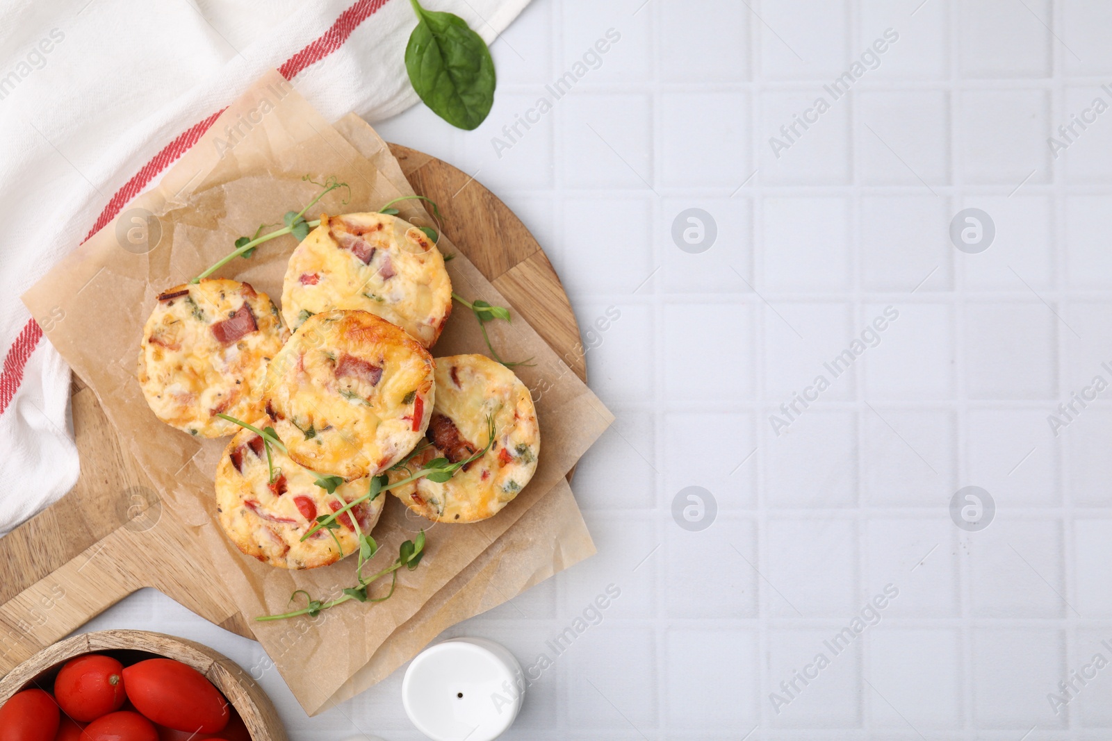 Photo of Delicious egg muffins with cheese and bacon on white tiled table, flat lay. Space for text