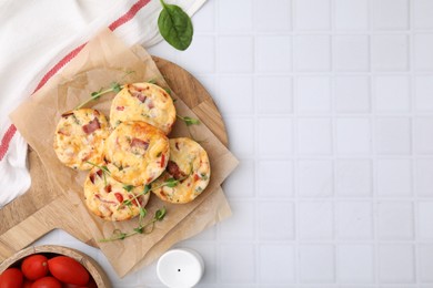 Photo of Delicious egg muffins with cheese and bacon on white tiled table, flat lay. Space for text