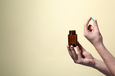 Man holding pill and bottle on beige background, closeup. Space for text