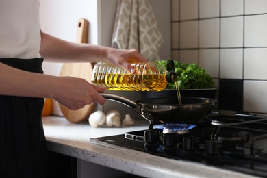 Photo of Vegetable fats. Woman pouring oil into frying pan on stove in kitchen, closeup