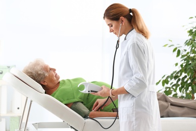 Doctor measuring blood pressure of elderly patient in hospital