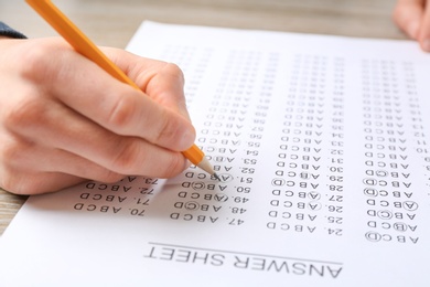 Student filling answer sheet at table, closeup