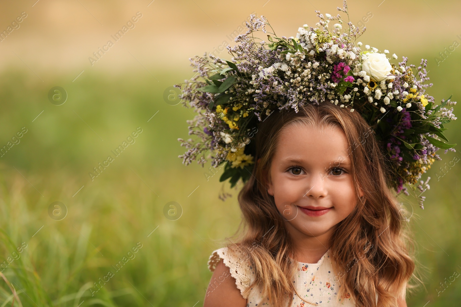 Photo of Cute little girl wearing wreath made of beautiful flowers in field