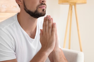 Photo of Religious man with clasped hands praying indoors, closeup. Space for text