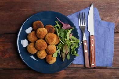 Photo of Delicious falafel balls with herbs on wooden table, flat lay