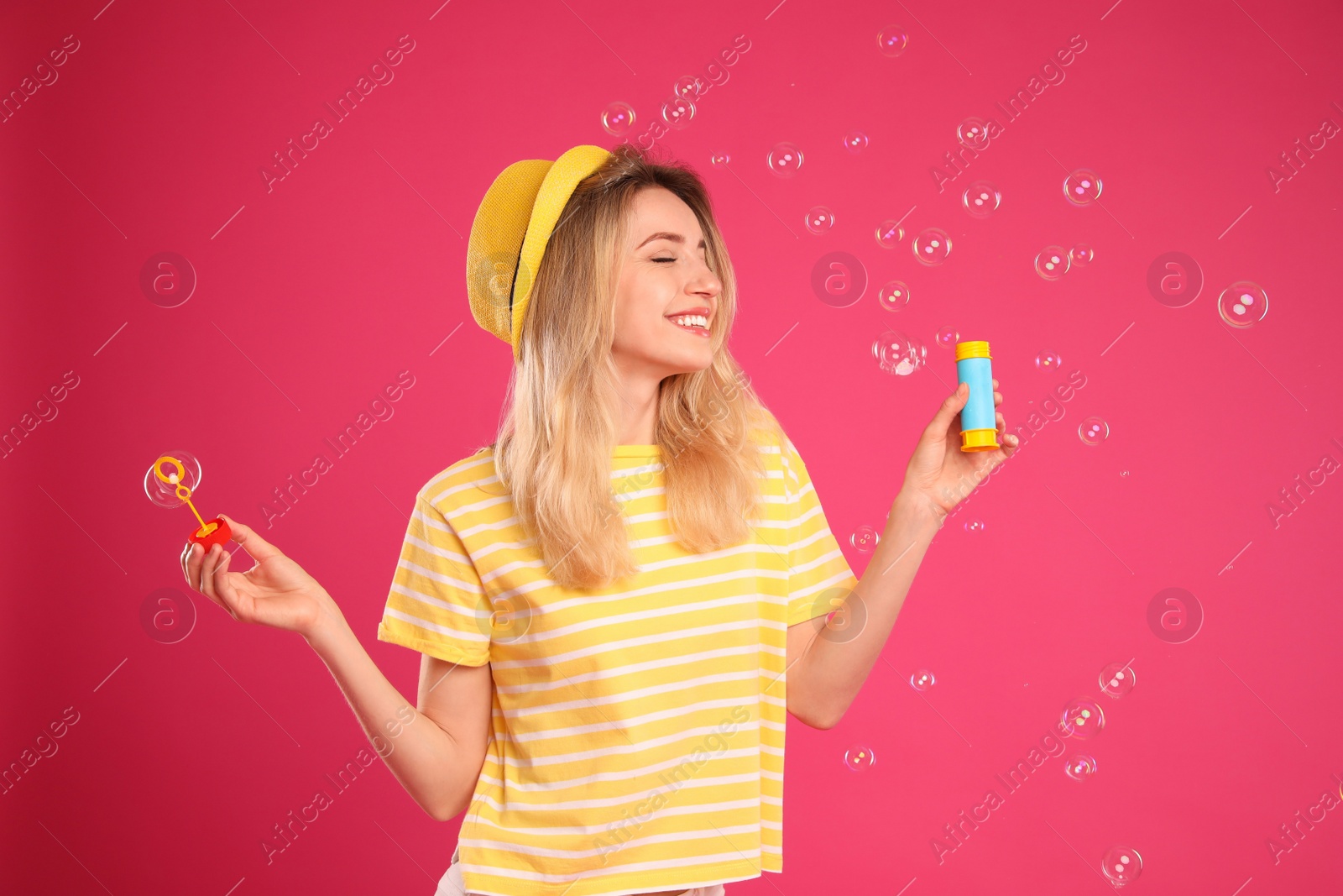 Photo of Young woman blowing soap bubbles on pink background