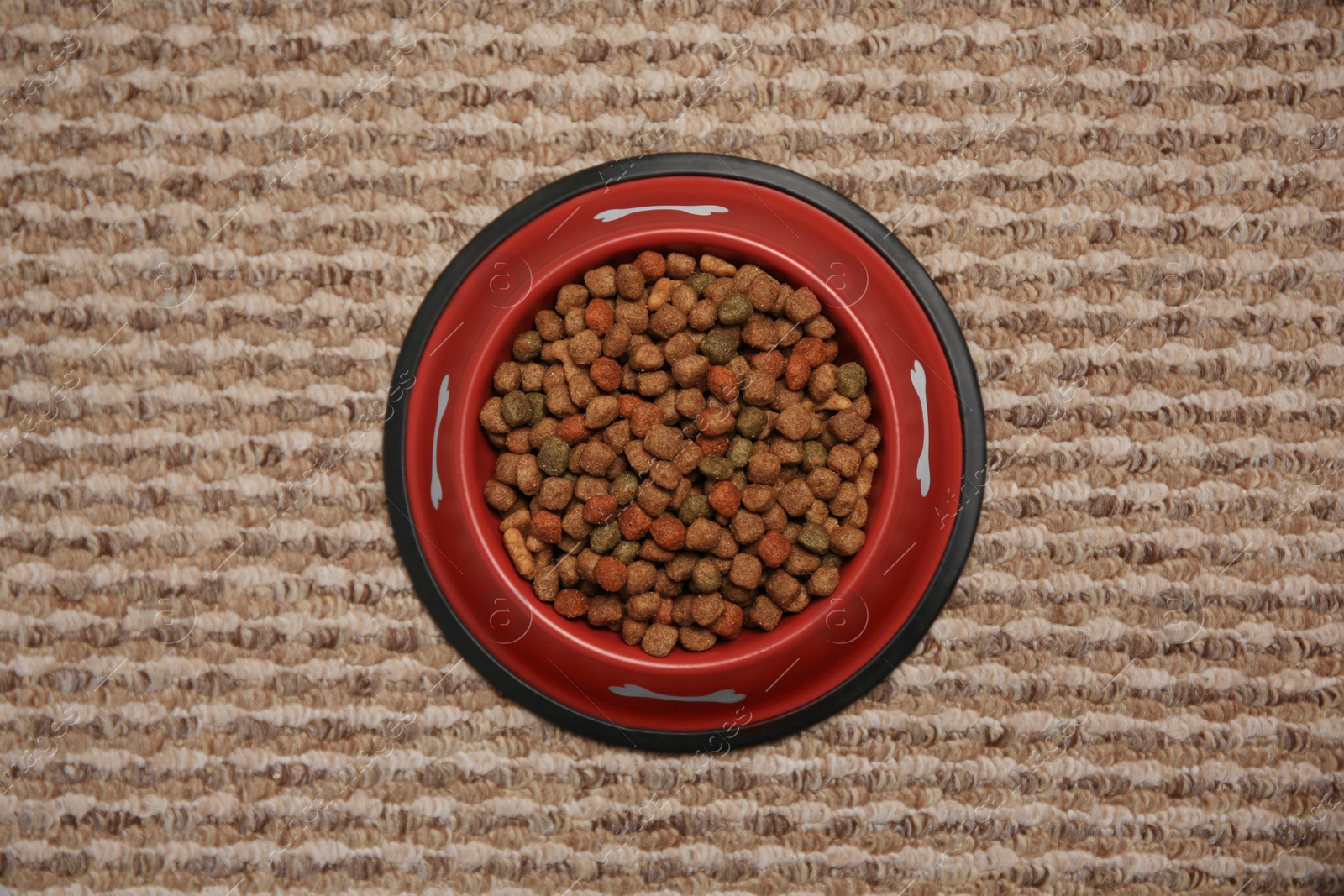 Photo of Dry dog food in feeding bowl on soft carpet, top view