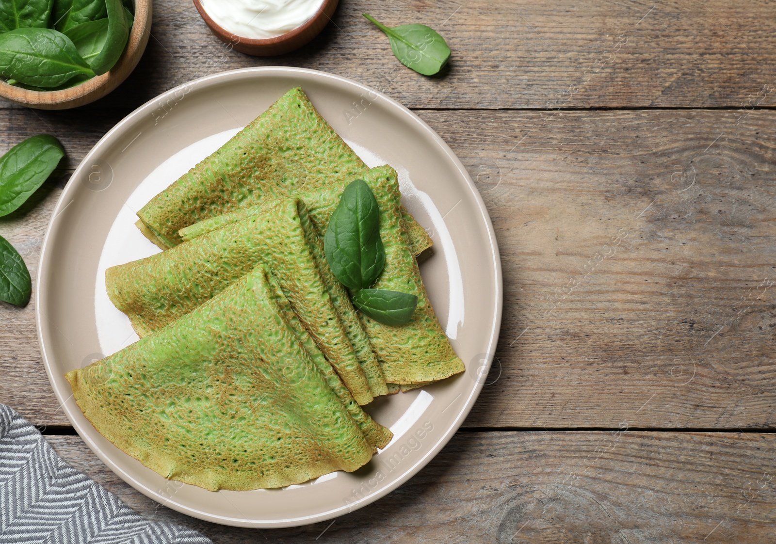 Photo of Delicious spinach crepes served on wooden table, flat lay. Space for text