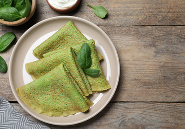 Delicious spinach crepes served on wooden table, flat lay. Space for text