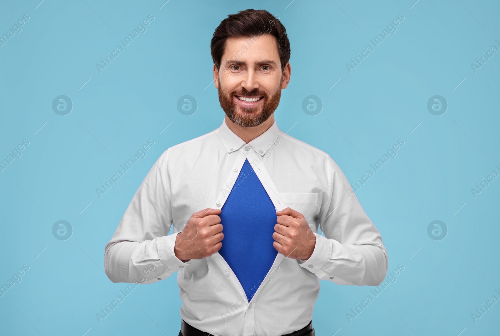 Photo of Happy businessman wearing superhero costume under suit on light blue background