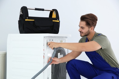 Photo of Young handyman fixing washing machine at home. Laundry day