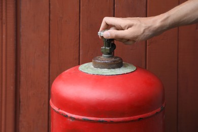 Photo of Man opening red gas cylinder near brown wooden wall, closeup