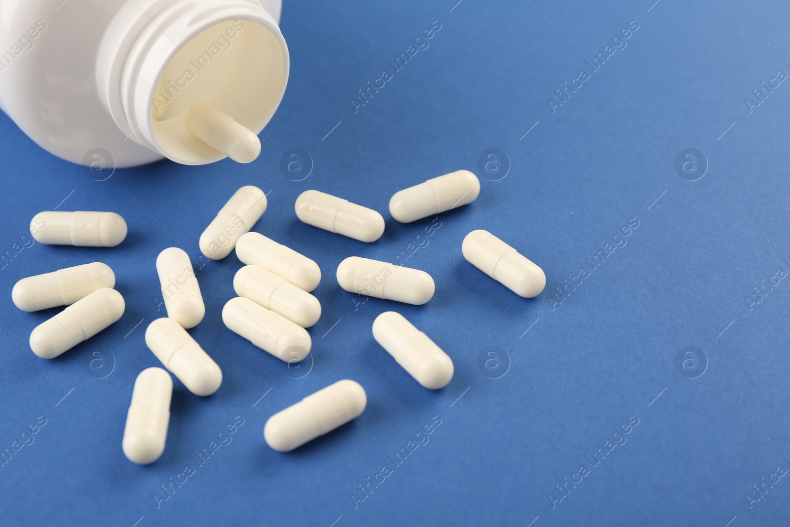 Photo of Bottle and vitamin capsules on blue background, closeup. Space for text