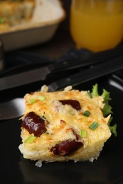 Photo of Tasty sausage casserole with green onions and cutlery served on table, closeup