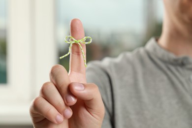 Man showing index finger with tied bow as reminder against blurred background, focus on hand