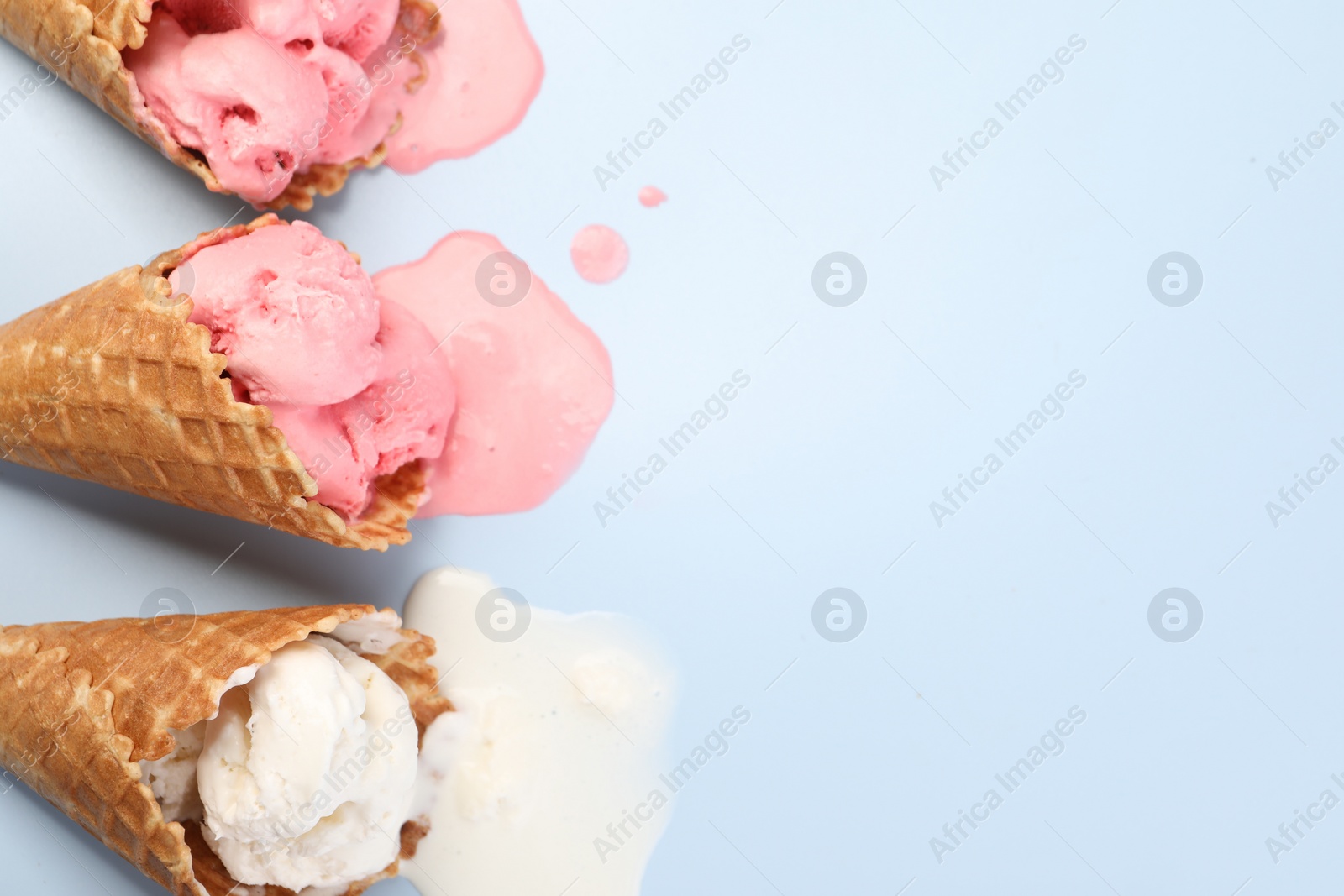 Photo of Melted ice cream in wafer cones on light blue background, flat lay. Space for text