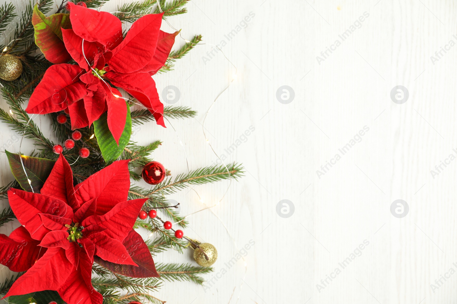 Photo of Flat lay composition with poinsettias (traditional Christmas flowers) and holiday decor on white wooden table. Space for text