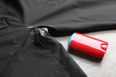 Black shirt with stain and deodorant on wooden background, closeup