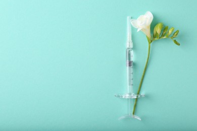 Cosmetology. Medical syringe and freesia flower on turquoise background, top view. Space for text