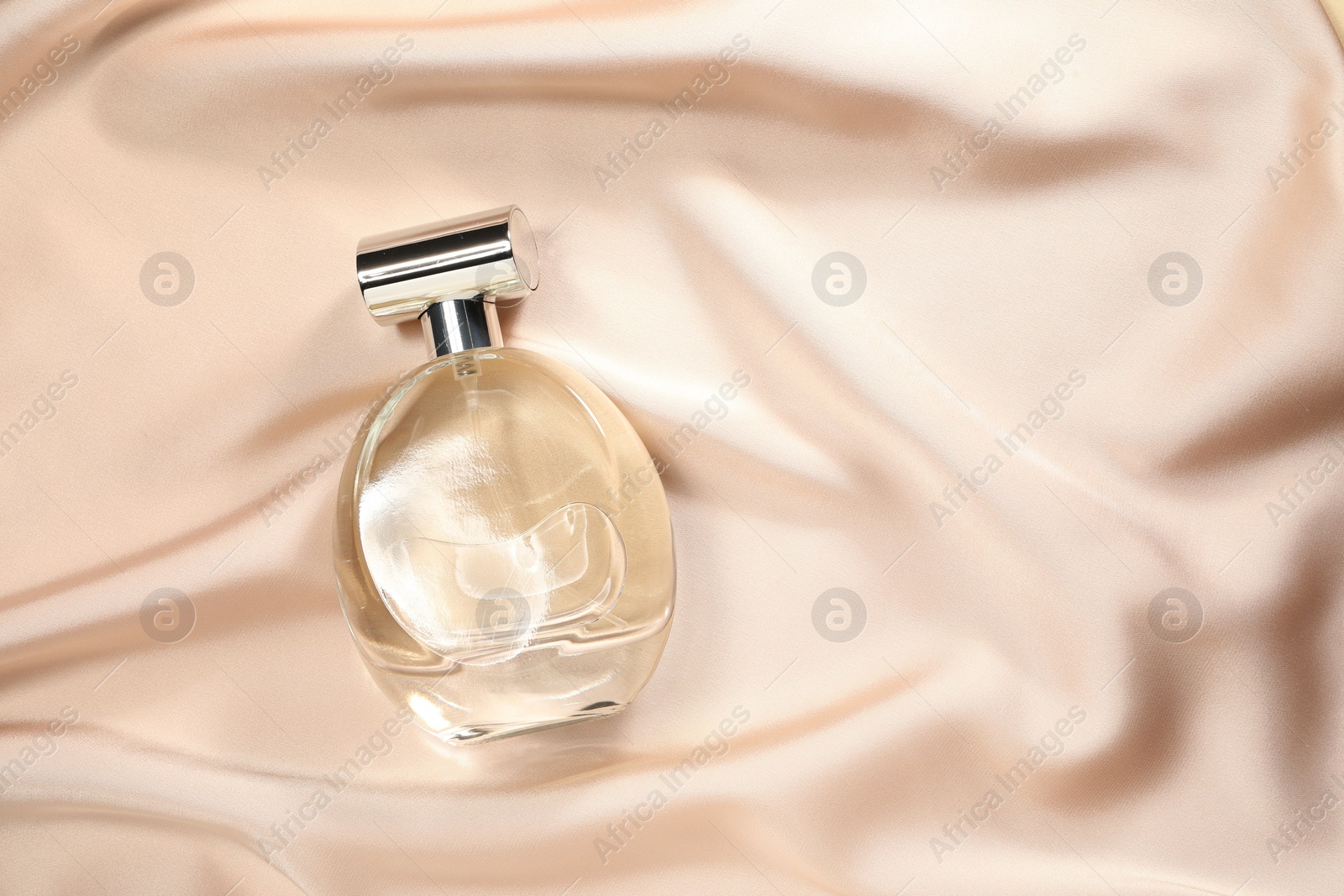 Photo of Luxury perfume in bottle on beige silk fabric, top view