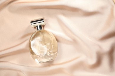 Luxury perfume in bottle on beige silk fabric, top view