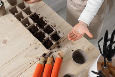 Photo of Little girl planting vegetable seeds into peat pots with soil at wooden table, closeup