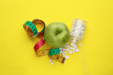 Photo of Weight loss pills, apple and measuring tape on yellow background, flat lay