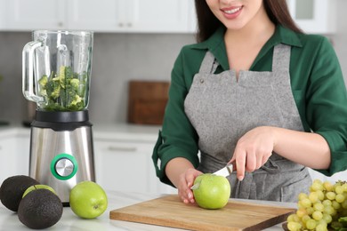Photo of Young woman cutting apple for smoothie at white table in kitchen, closeup