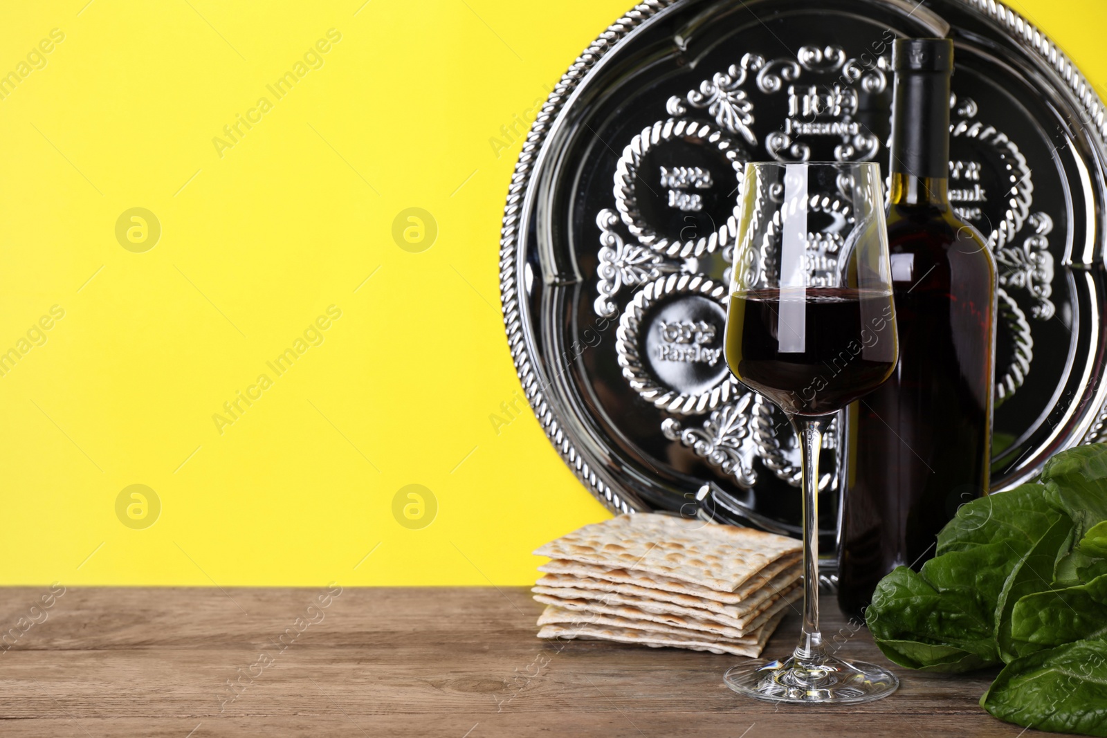 Photo of Symbolic Pesach (Passover Seder) items on wooden table against yellow background, space for text