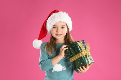 Photo of Cute child in Santa hat with Christmas gift on pink background