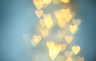 Photo of Blurred view of beautiful gold heart shaped lights on light blue background