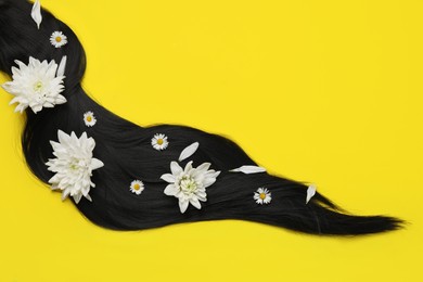 Lock of healthy black hair with flowers on yellow background, top view. Space for text