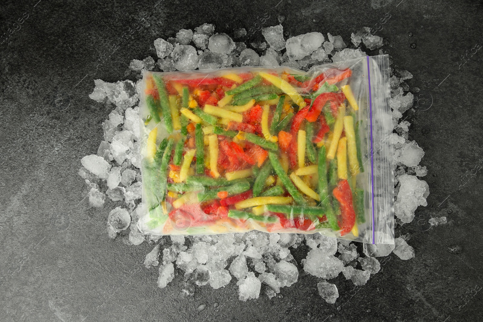 Photo of Zip bag with different frozen vegetables and ice on grey table, top view