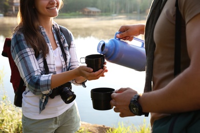 Photo of Man pouring drink into mug for young woman outdoors. Camping season