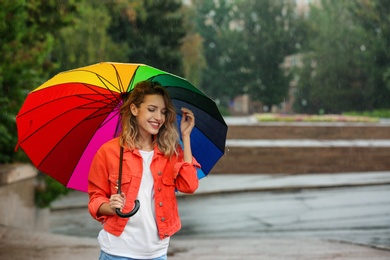 Happy young woman with bright umbrella under rain outdoors