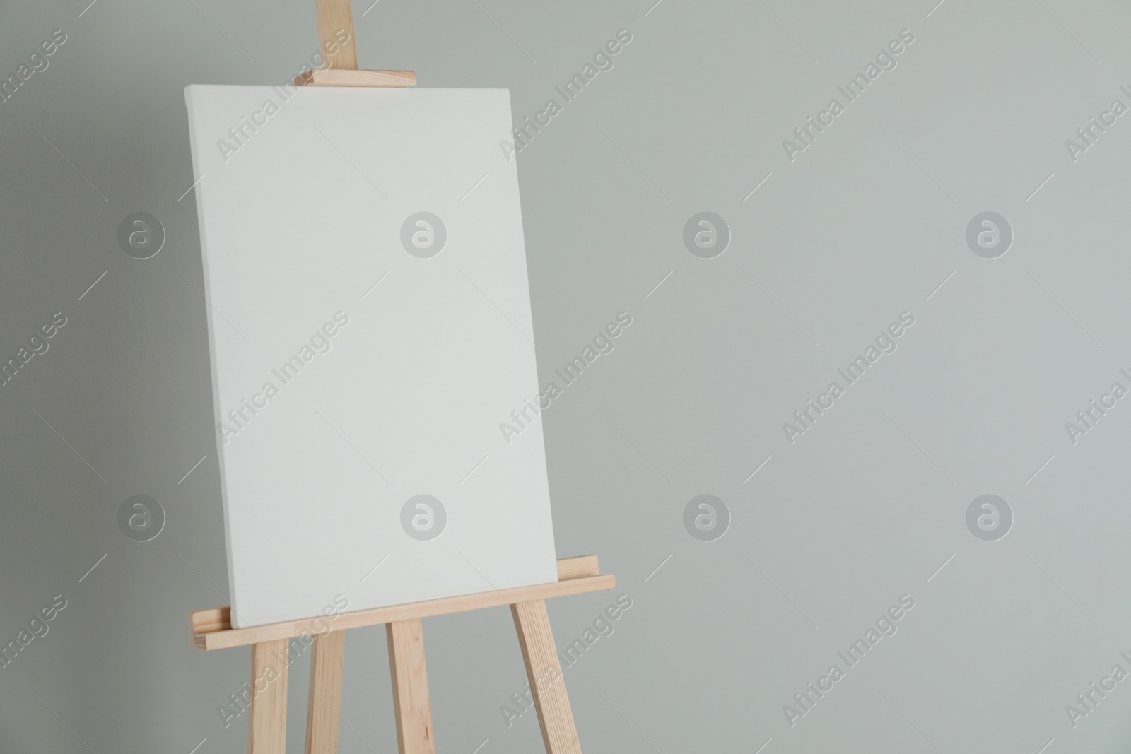 Photo of Wooden easel with blank canvas on light background. Space for text