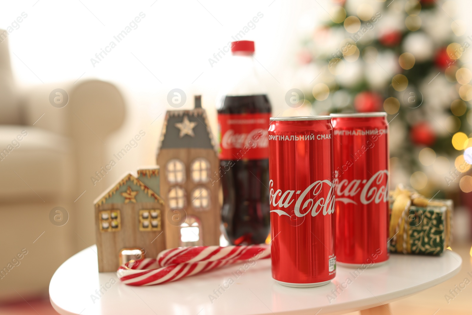 Photo of MYKOLAIV, UKRAINE - JANUARY 15, 2021: Coca-Cola cans and bottle near gift box on table with Christmas decor