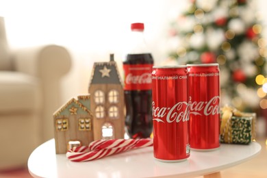 MYKOLAIV, UKRAINE - JANUARY 15, 2021: Coca-Cola cans and bottle near gift box on table with Christmas decor