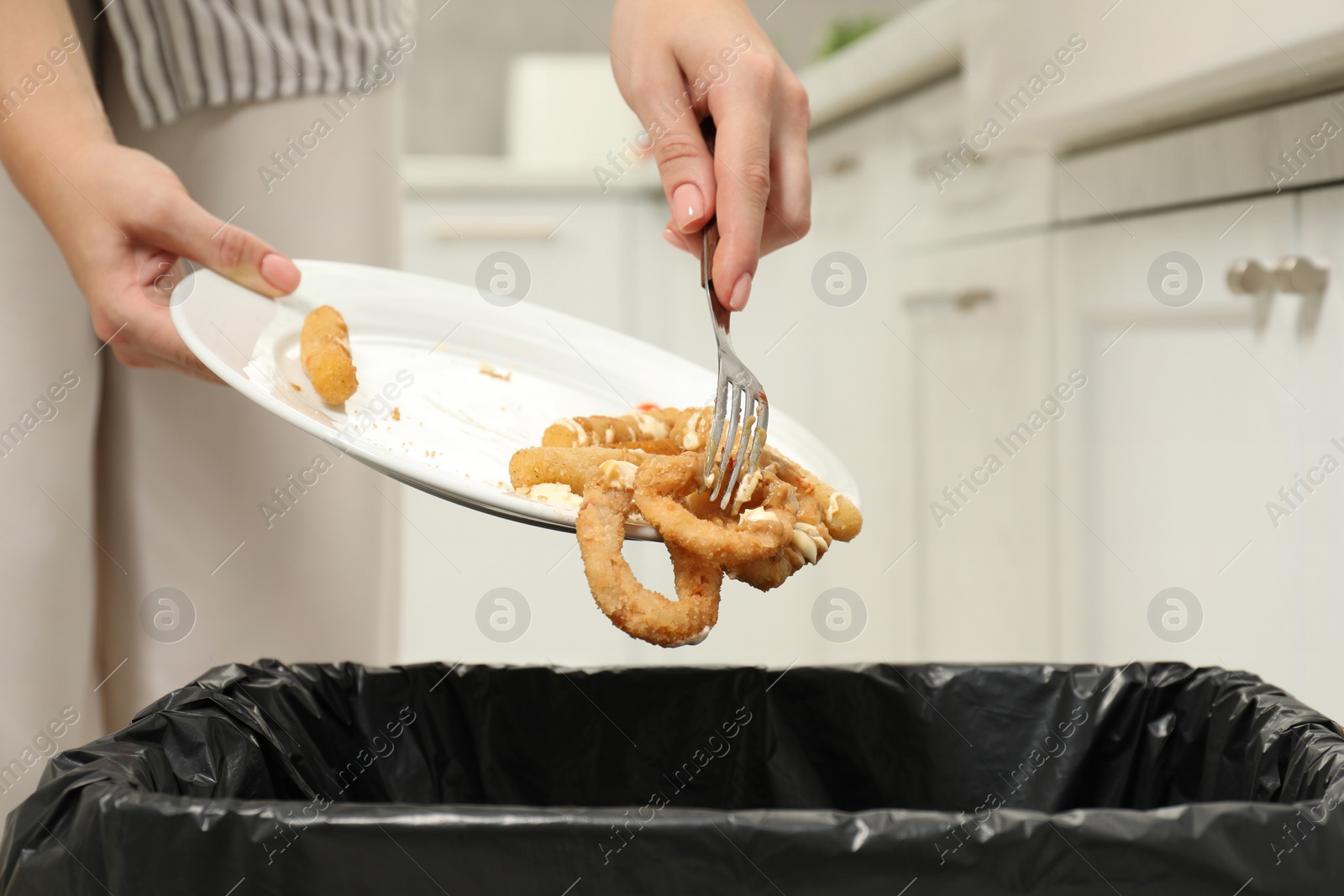 Photo of Woman throwing onion rings into bin indoors, closeup