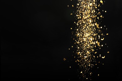 Photo of Shiny golden glitter falling down on black background, space for text. Bokeh effect