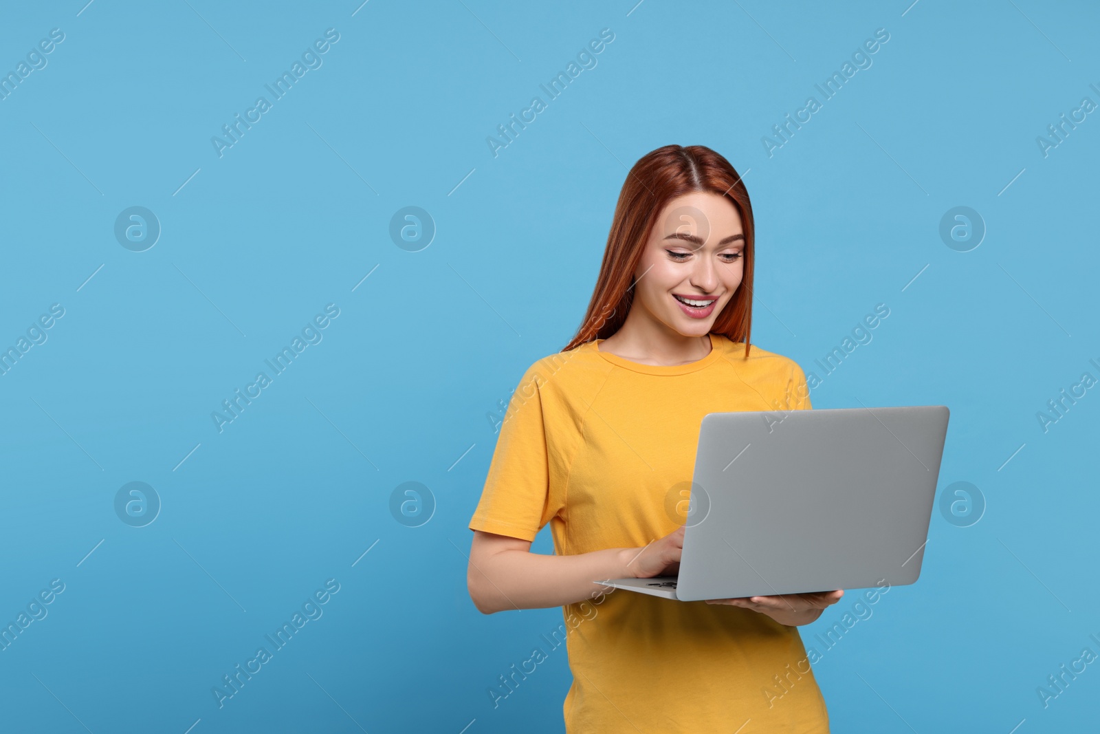 Photo of Smiling young woman working with laptop on light blue background, space for text