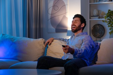 Photo of Laughing man watching TV on sofa at home, space for text