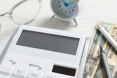 Photo of Calculator, money, pencils and alarm clock on white wooden table, closeup. Tax accounting