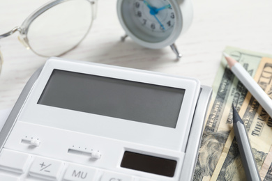 Calculator, money, pencils and alarm clock on white wooden table, closeup. Tax accounting